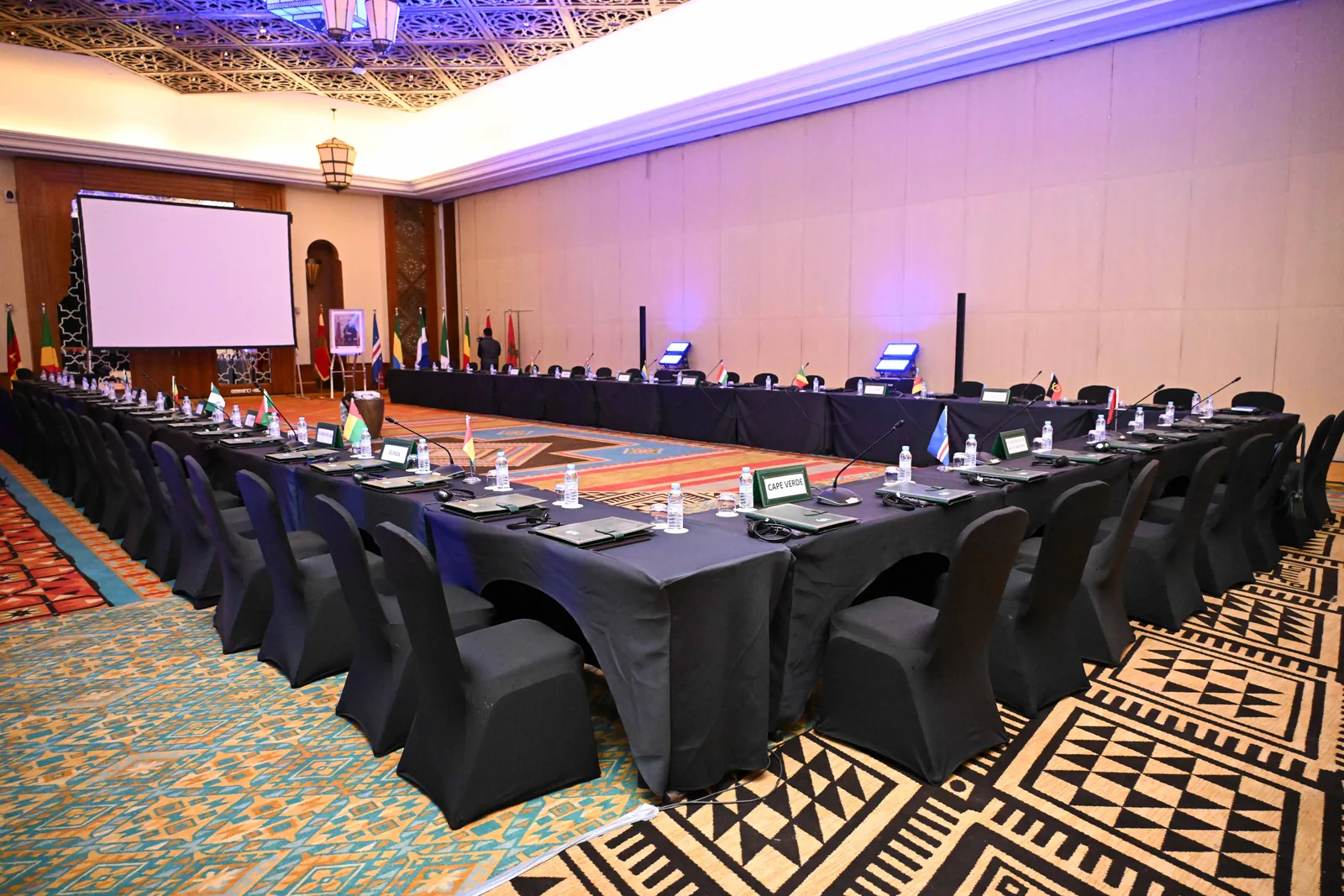 Salle de conférence équipée de tables, micros et écran de projection.